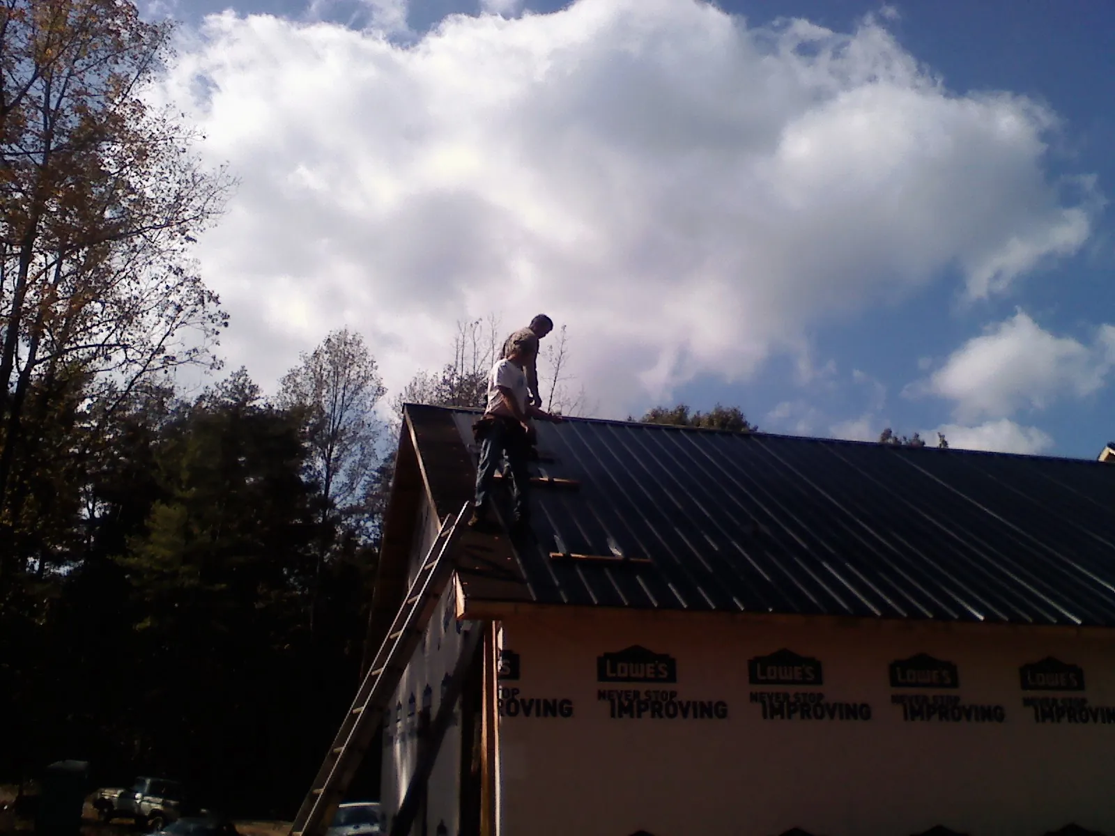 Roofer fastening dark metal panels high against a cloudy sky, from a Roof Inspection job in Naches