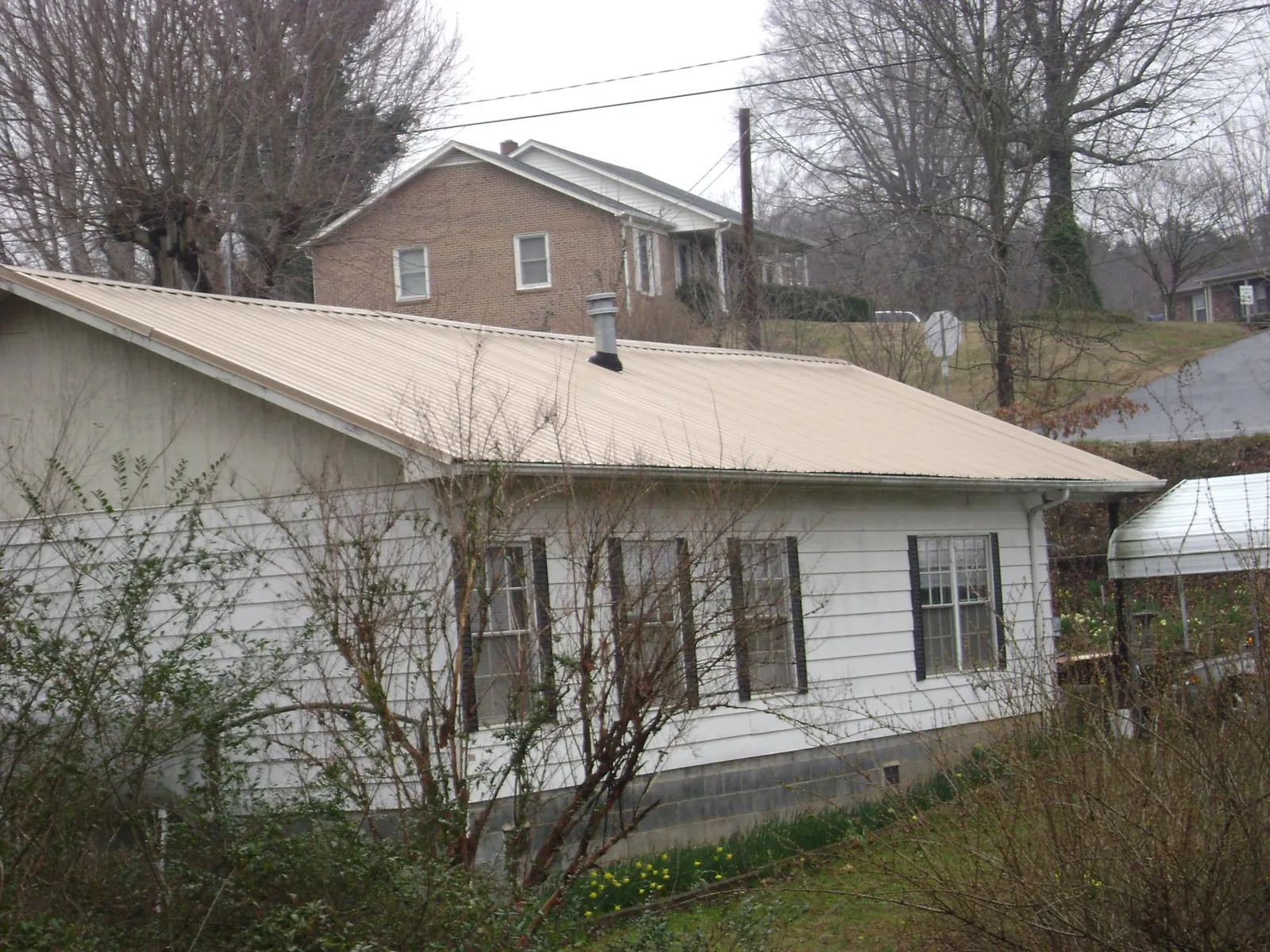 Tan metal roof on a white sided house set into a hillside — Commercial Roofing by Roofing Brothers in Naches